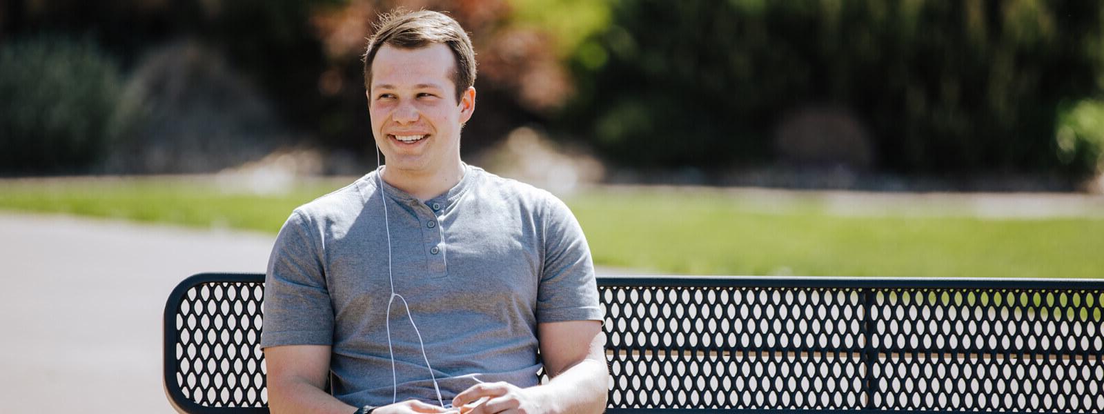 男学生戴着耳机坐在长凳上微笑